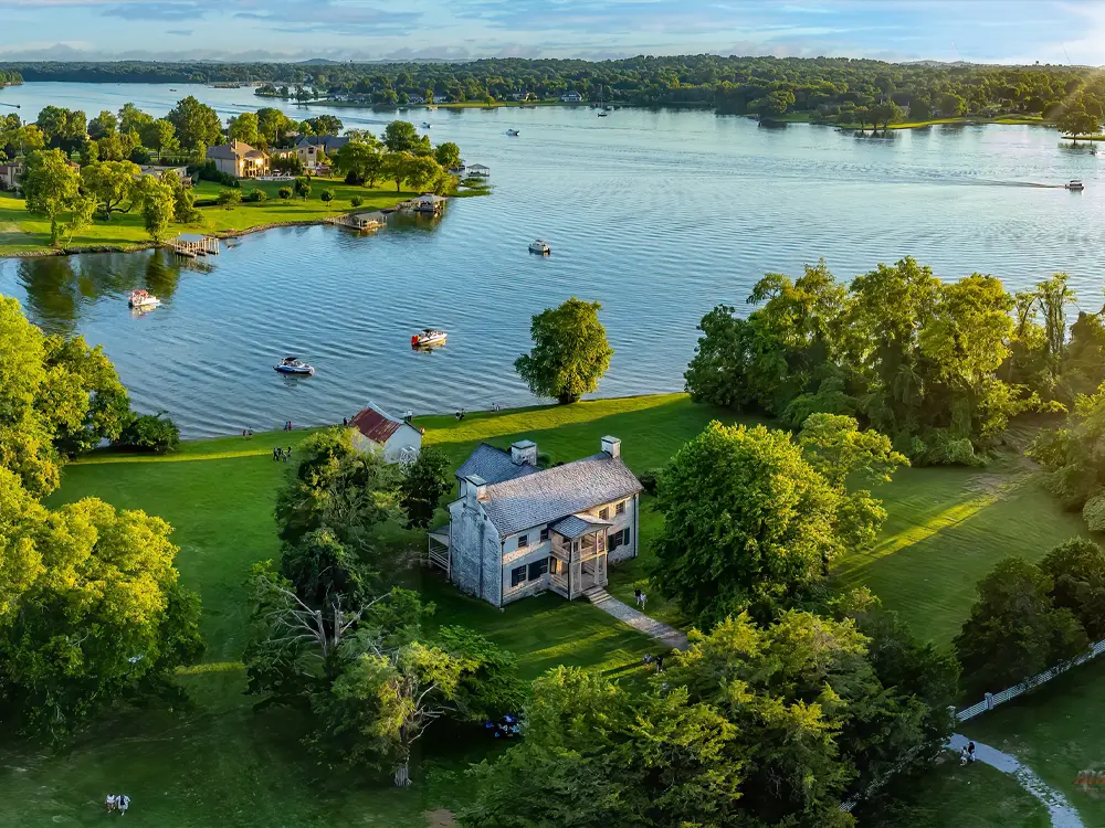 Aerial view of a waterfront property with a large house, lush green lawn, trees, and a scenic lake with boats, ideal for luxury real estate and peaceful living. Rock Castle, Hendersonville TN