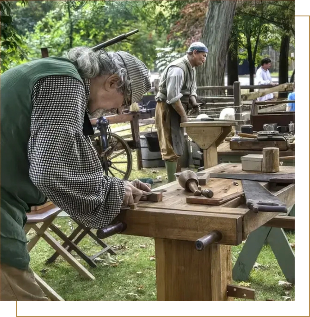 Historical reenactor woodworking outdoors at traditional crafts fair, demonstrating antique carpentry techniques with vintage tools and period costume, educational heritage event with trees in background. Rock Castle, Hendersonville TN