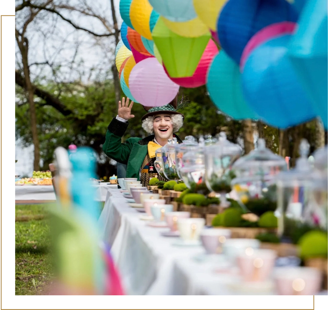 Colorful outdoor party with festive decorations, balloons, and a costumed entertainer waving near a long table set for an event in a park setting. Rock Castle, Hendersonville TN