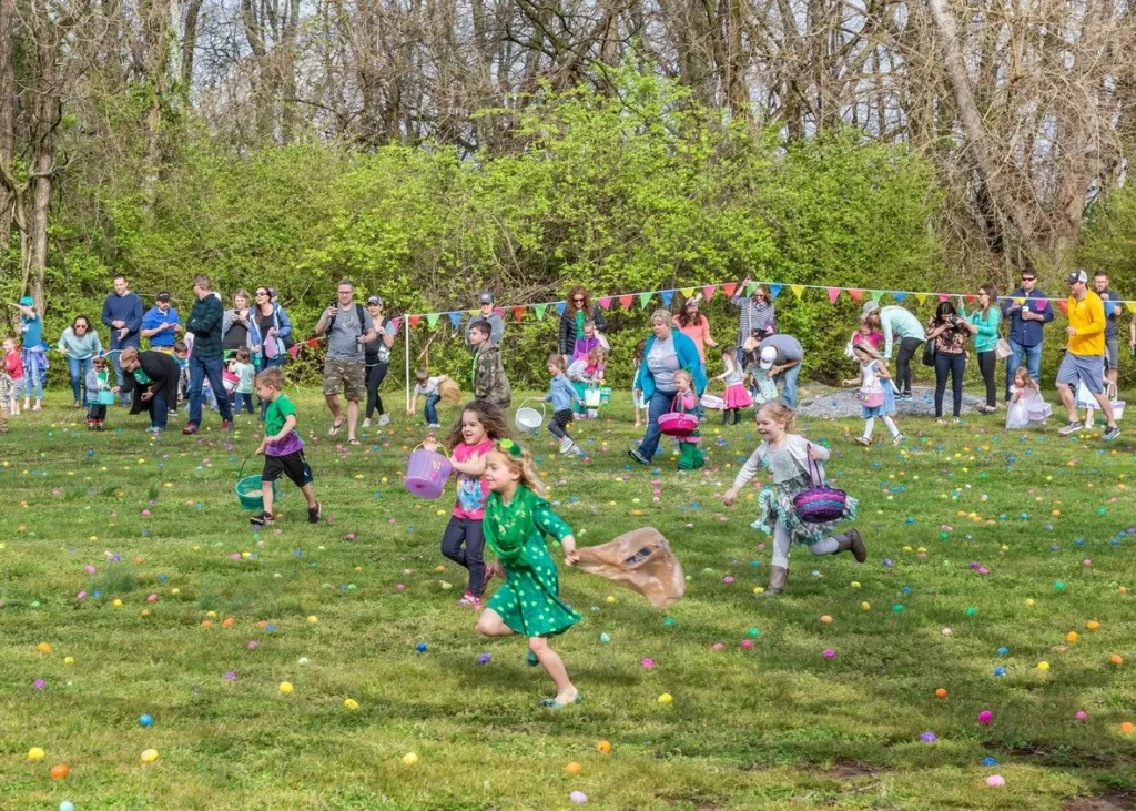 Young children running across a grassy lawn filled with colorful eggs during a Wonderland Egg Hunt event at Historic Rock Castle.