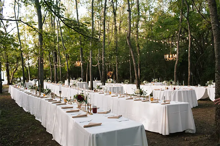 Image of dining tables for a wedding reception in the woods by the lake.